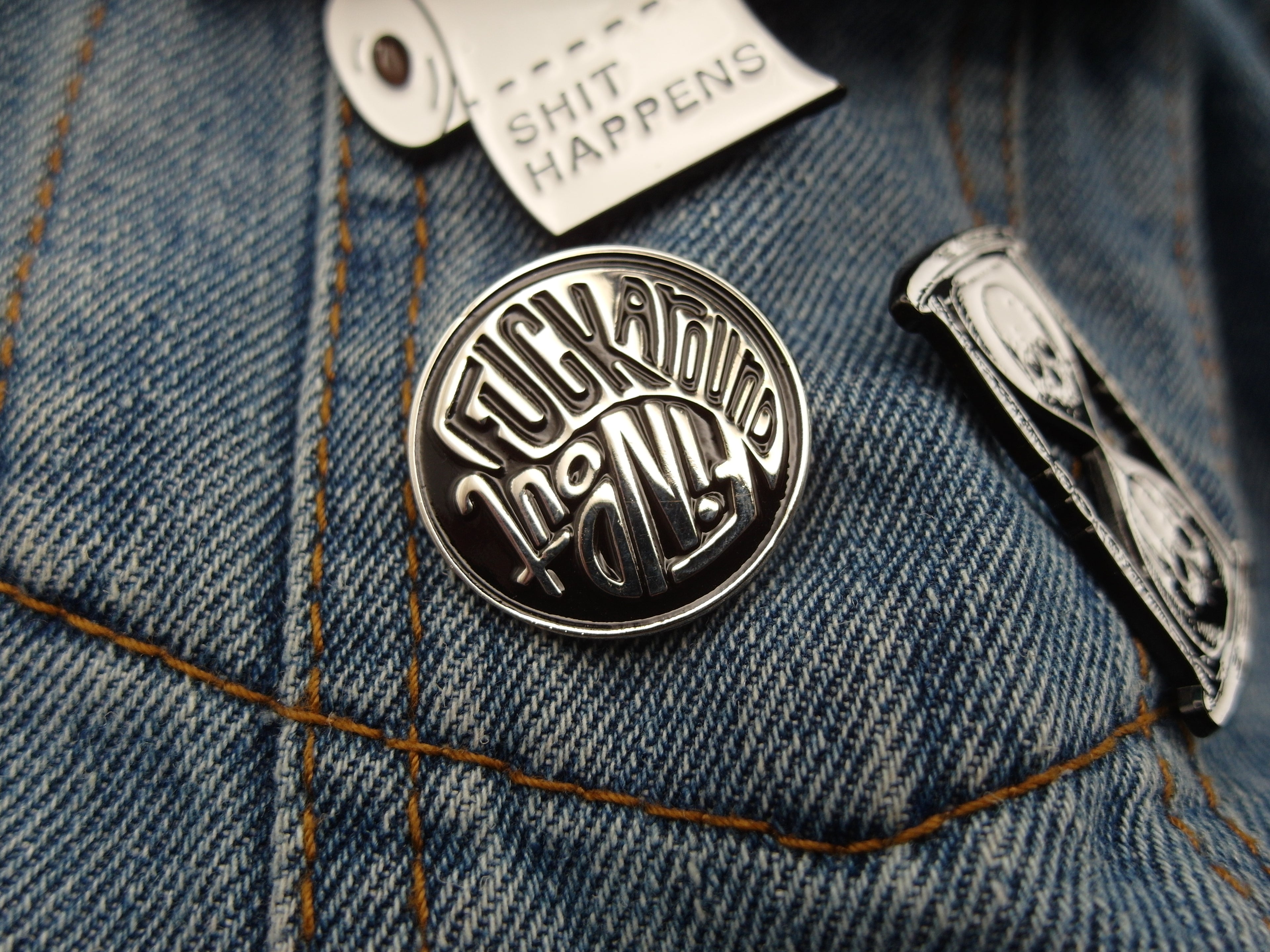 a black a silver enamel pin badge that reads "f*ck around, find out" in the style of a yin yang shape.