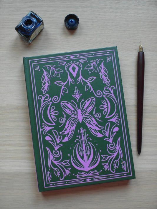 Green and pink hardback journal featuring designs of floral flourishes and swirls around a central butterfly - image decor of a pen and ink pot